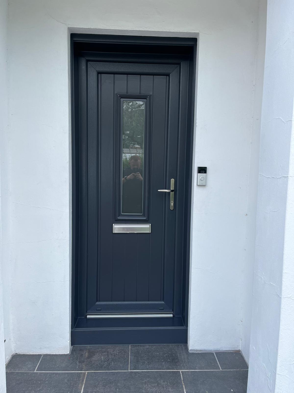 Anthracite composite door with a slim vertical glass slot on a white render house