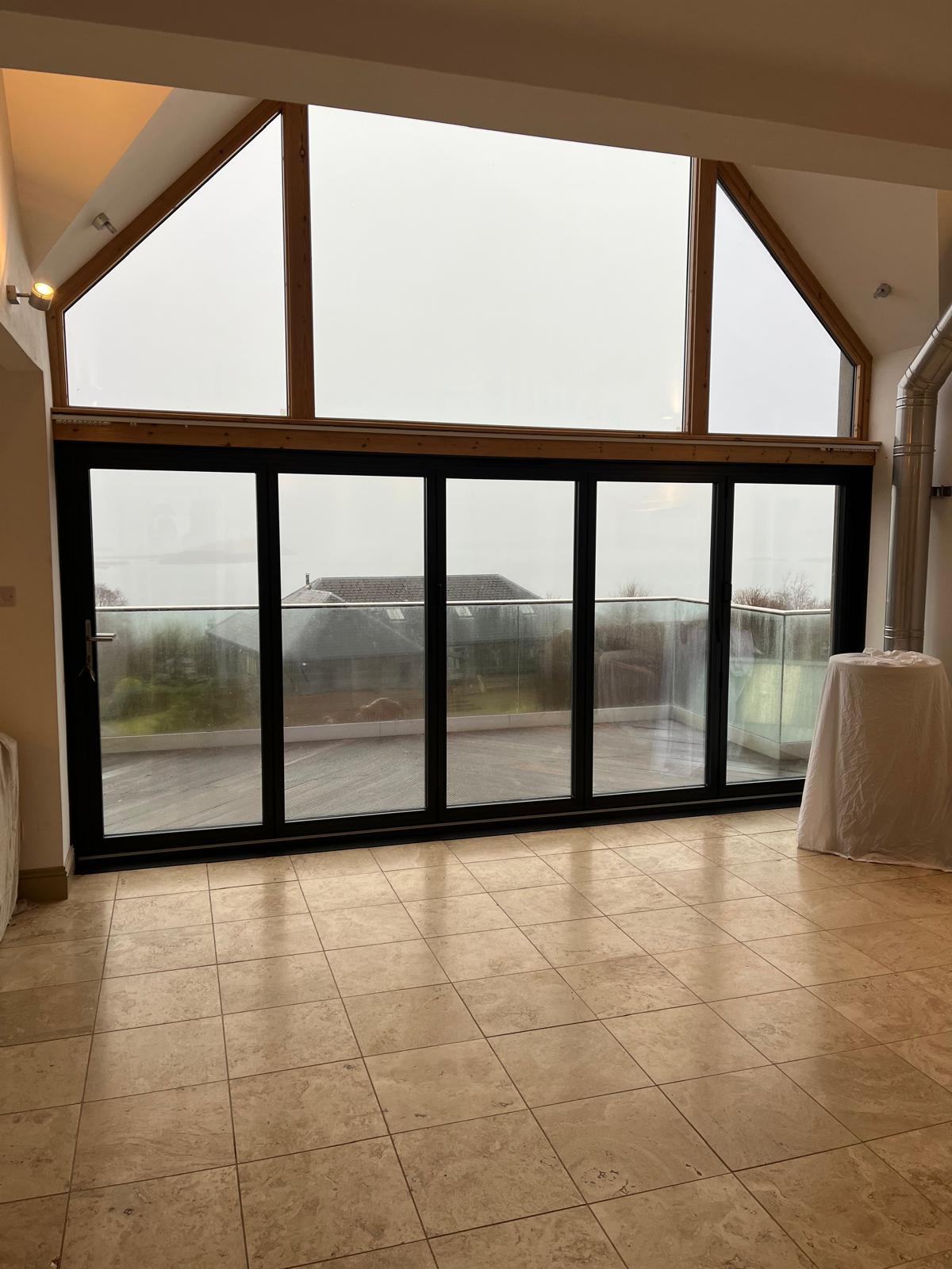 Five-panel black bifold doors under a triangular apex window opening onto a balcony
