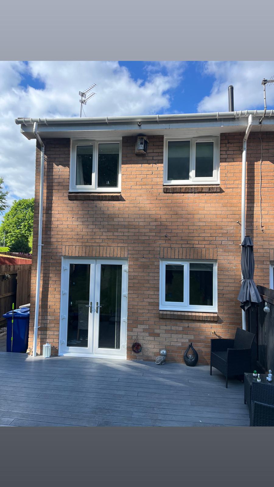 Two-storey brick house rear with anthracite windows and French doors on a sunny day